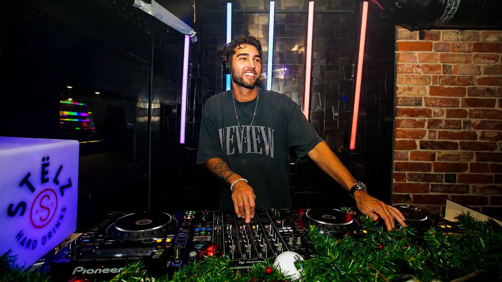 Een DJ draait lachend achter zijn set in een club met neonbuizen