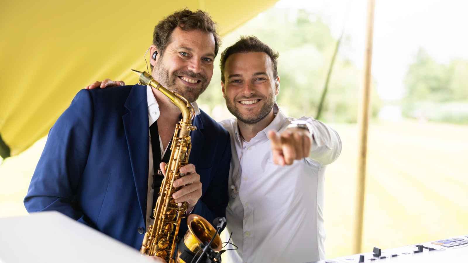 Een saxofonist en een DJ poseren samen achter de set tijdens een buitenevenement