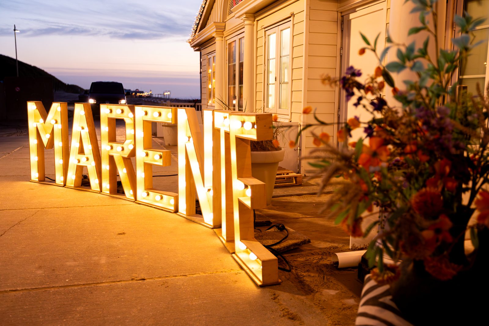 Grote lichtletters met de naam Marente op het strand bij zonsondergang