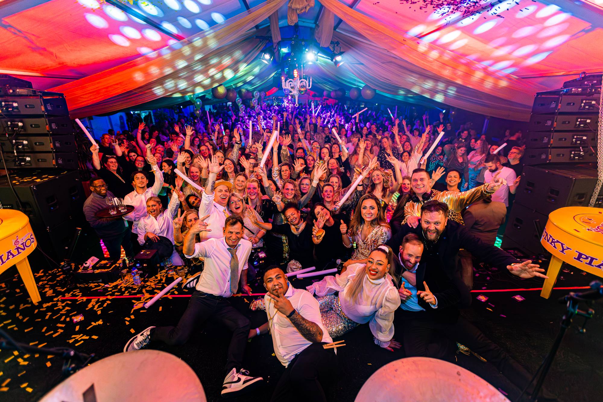 Funky Pianos en gasten poseren samen voor de camera op het podium, met een volle tent erachter