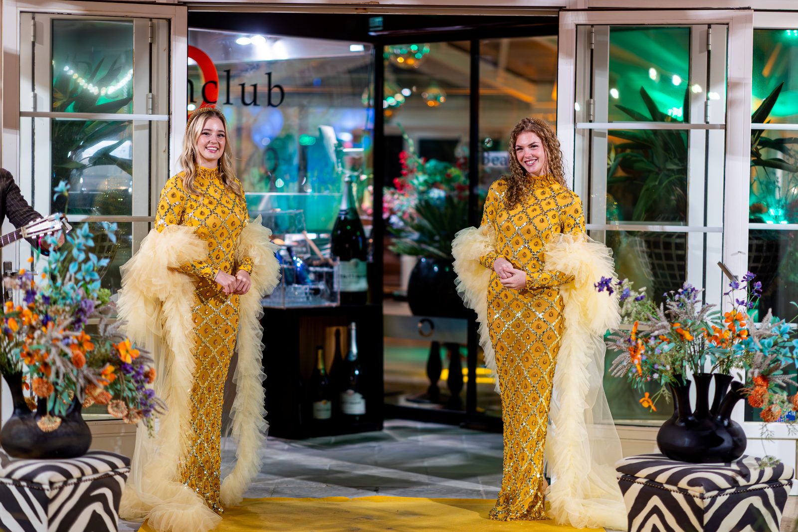 Twee hostessen in gouden jurken met veren bij de ingang van de beachclub
