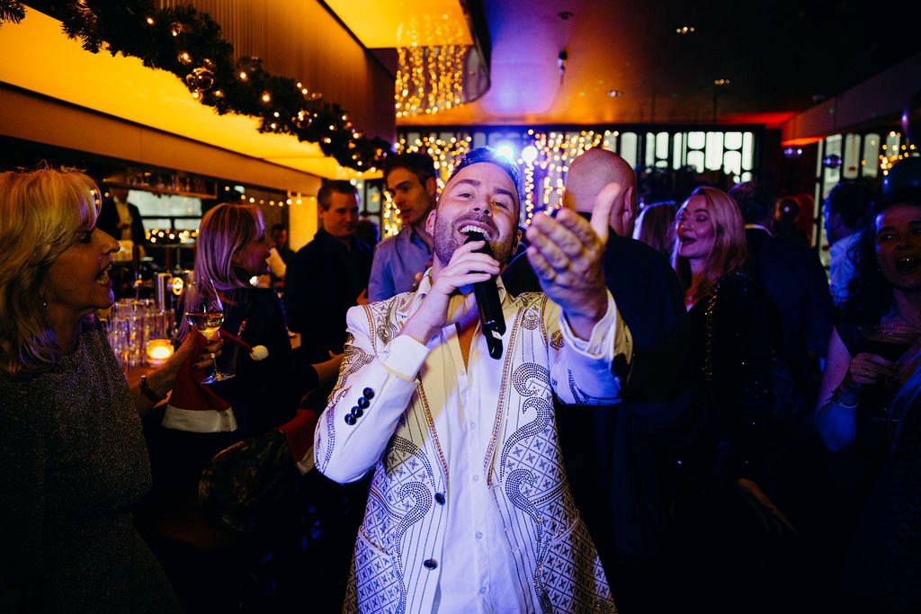 Zanger Menzo zingt in een wit jasje tussen de gasten