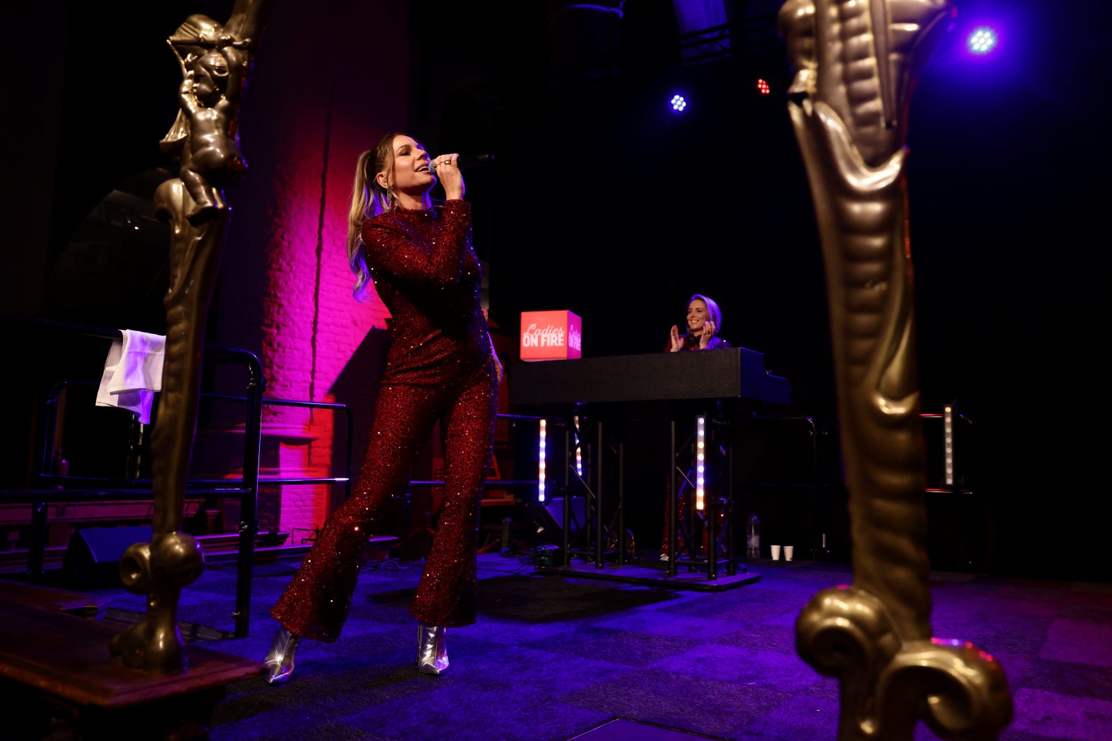 Een zangeres van Ladies on Fire in een rood glitterpak op het podium tussen gouden beelden