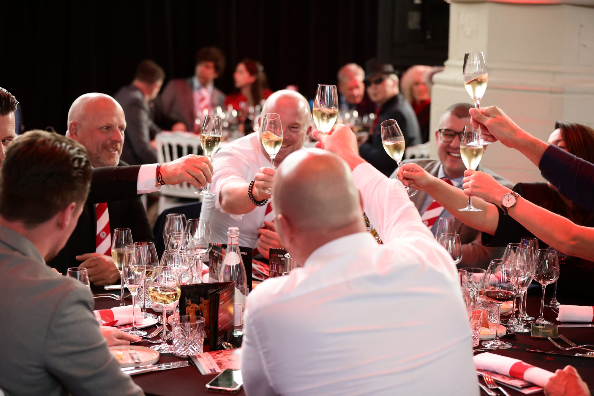 Gasten proosten aan tafel met een glas in de hand tijdens het Rood-Witte Mannen & Vrouwen Diner