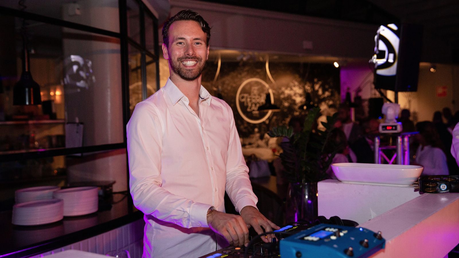 Een lachende DJ achter zijn mengpaneel tijdens een avondfeest