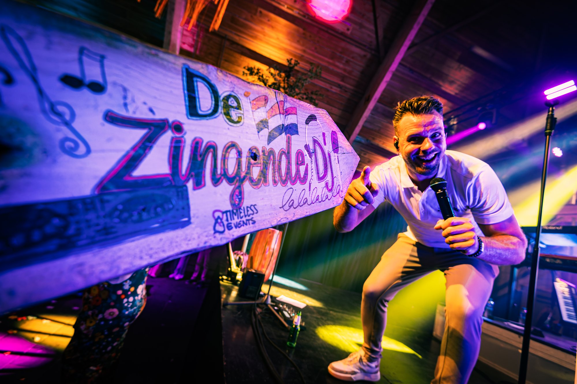 De Zingende DJ zingt in de microfoon naast een houten bord met zijn naam