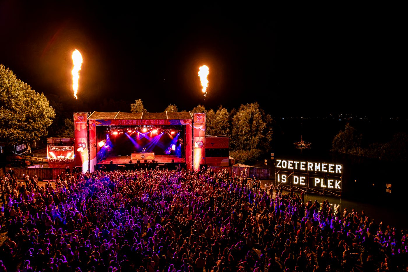 Een festivalpodium met vlammen en een publiek in paars licht